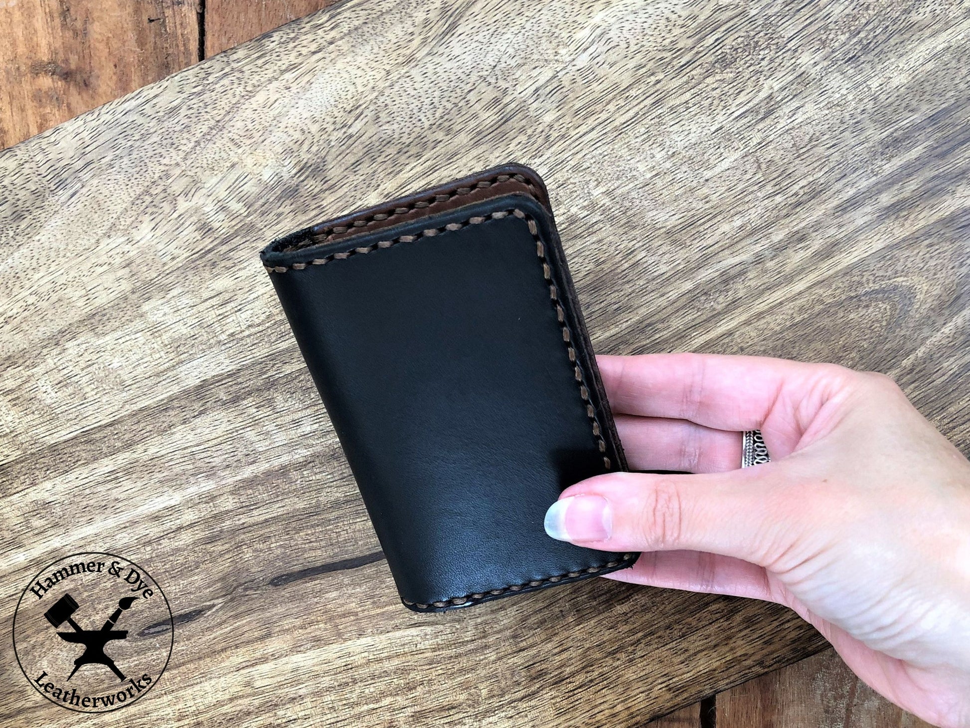 Handmade Two-tone Bifold Leather Card Wallet in Black and Brown with brown stitching held in a hand