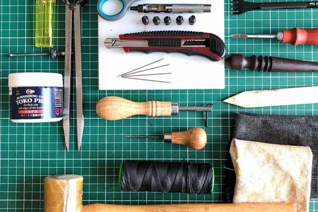 a selection of beginner leathercraft tools layed out on a green self-healing cutting mat