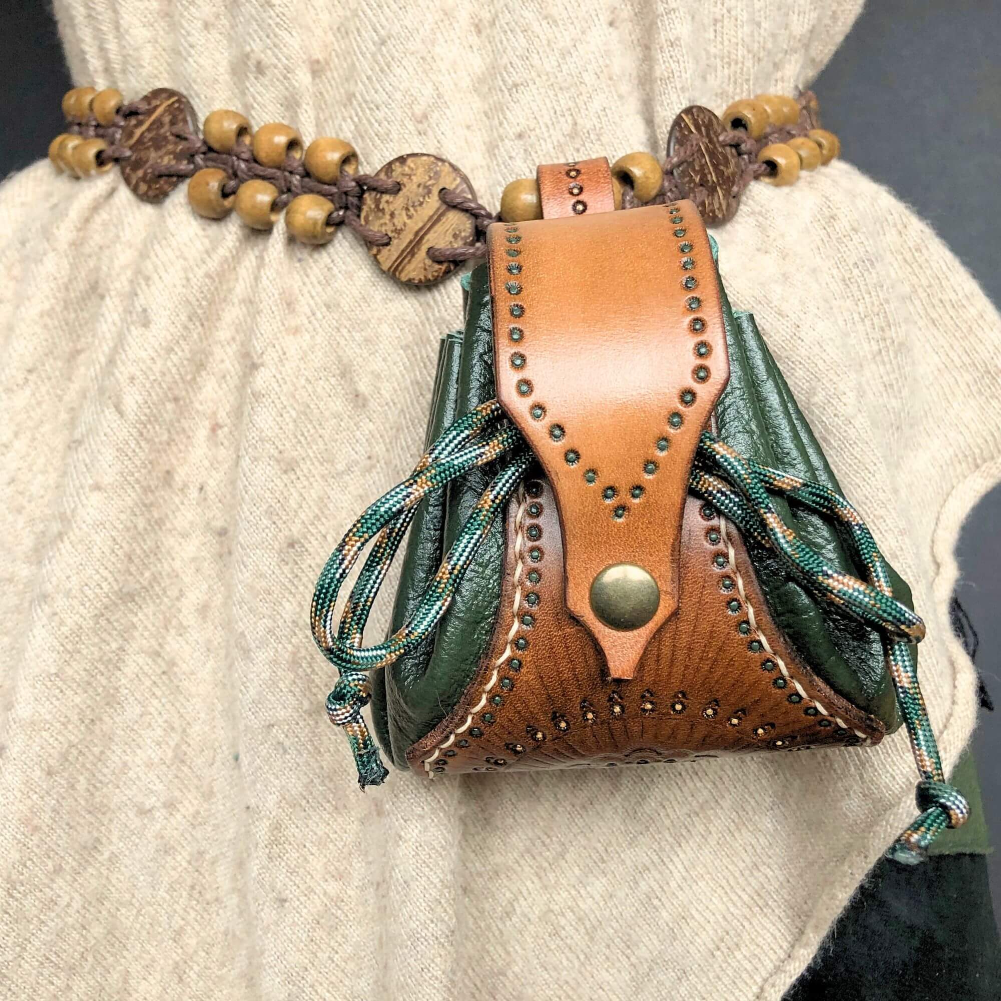 brown and green tooled drawstring leather pouch worn on a belt