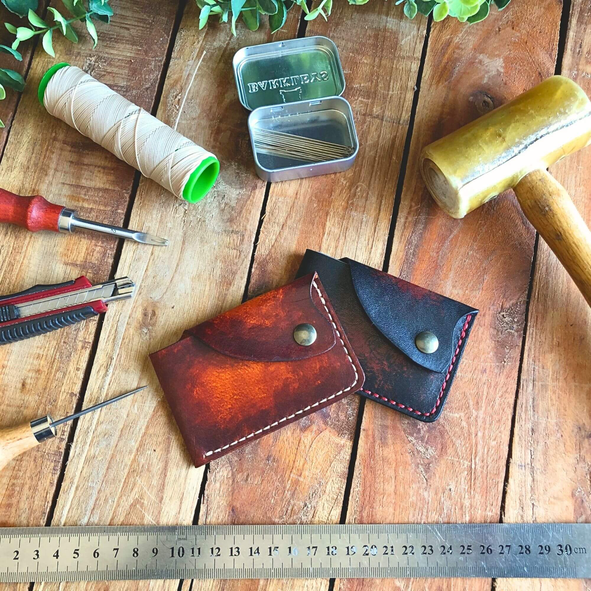 2 compact leather card wallets surrounded by leathercraft tools
