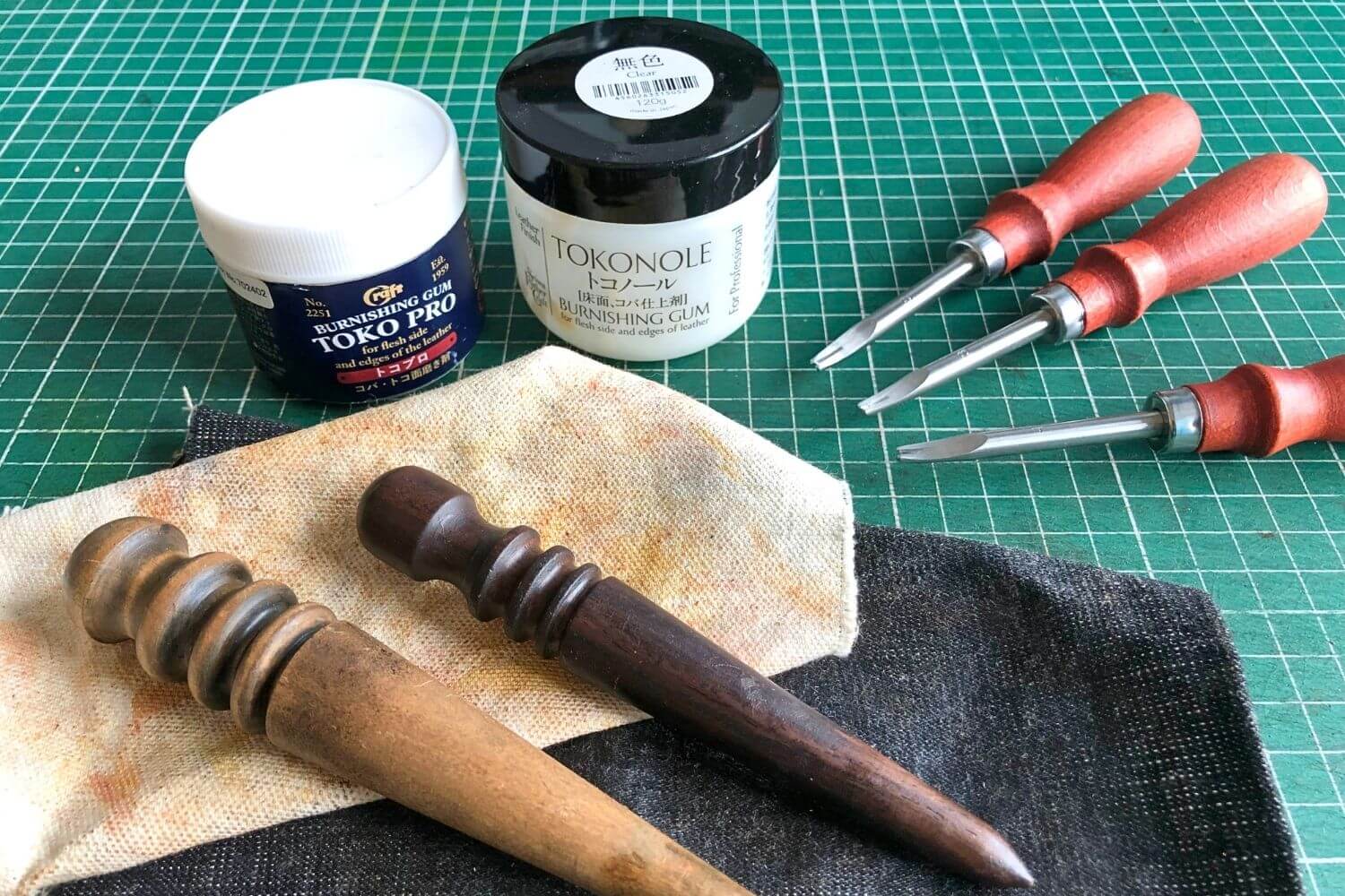 The Beginner's Leathercraft Tool Guide 5 Edge bevelers, burnishing compounds tokonole and toko pro plus 2 wooden slickers and canvas on a green self-healing cutting mat