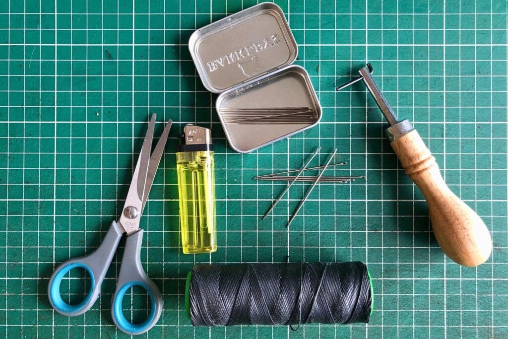 The Beginner's Leathercraft Tool Guide 4 Scissors, lighter, threand and needles and a stitch groover on a self-healing cutting mat