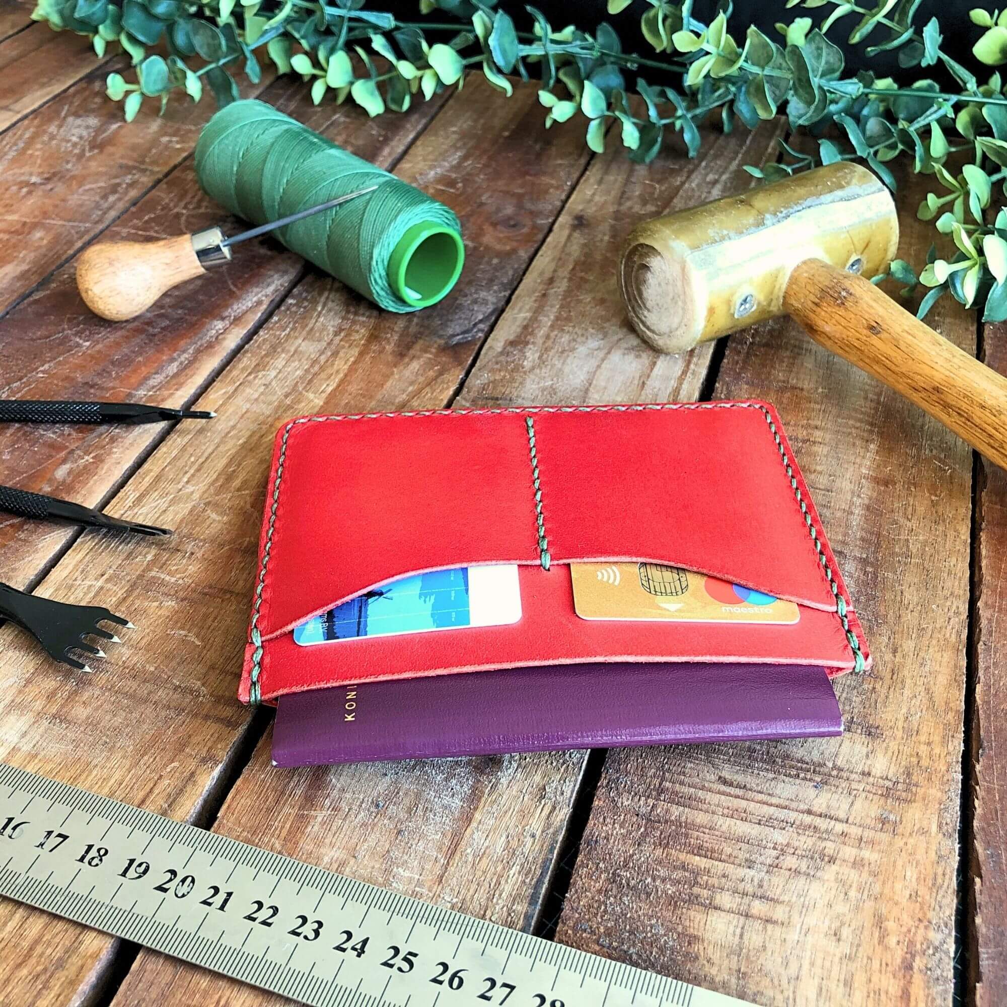 Compact Passport Cover 5 red leather passport wallet surrounded by leathercraft tools on a rustic wooden background