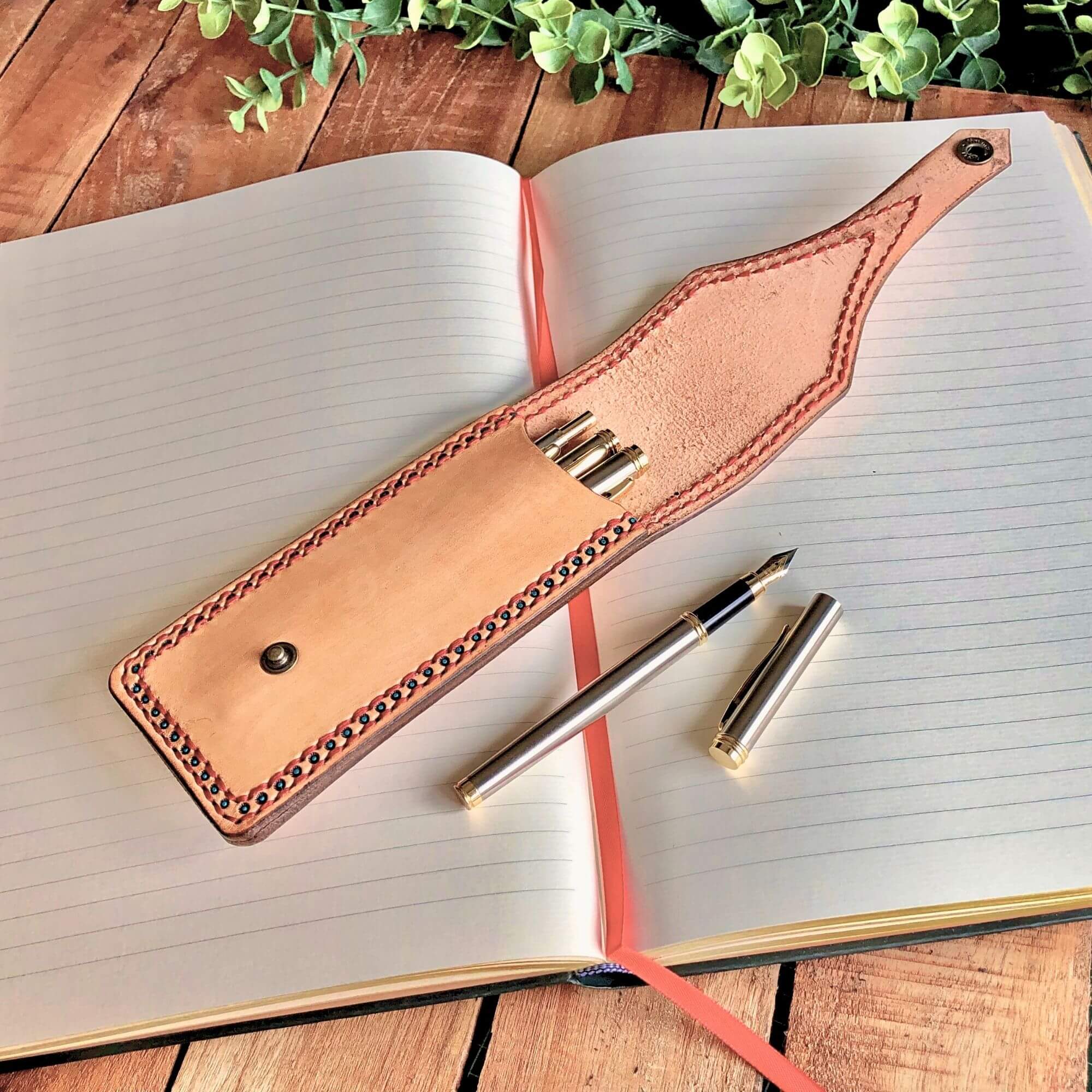 Leather Pen pouch with decorative stitching with pens inside on an open notebook