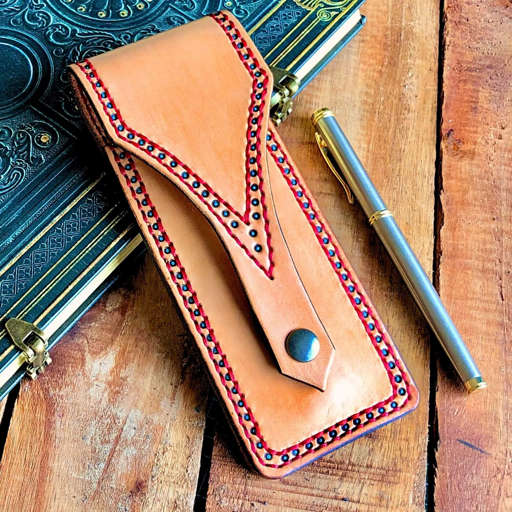 Leather Pen pouch with decorative stitching and embossed details with a pen and a notebook on a rustic wooden surface