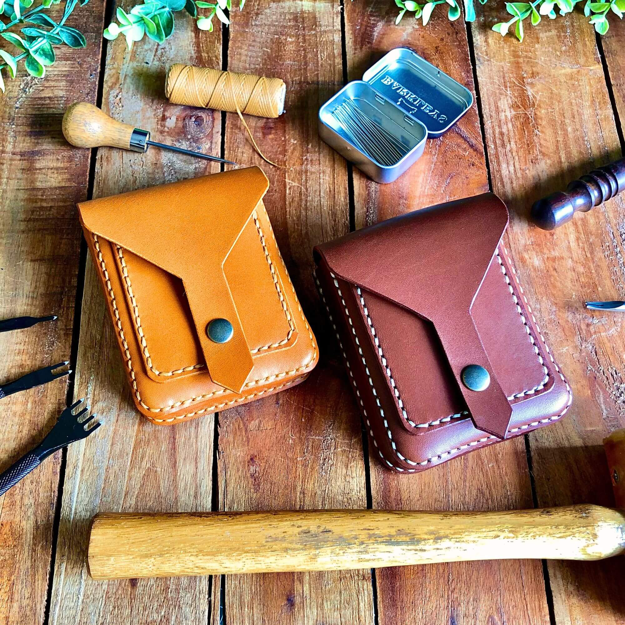 two compact leather belt pouches surrounded by leathercraft tools